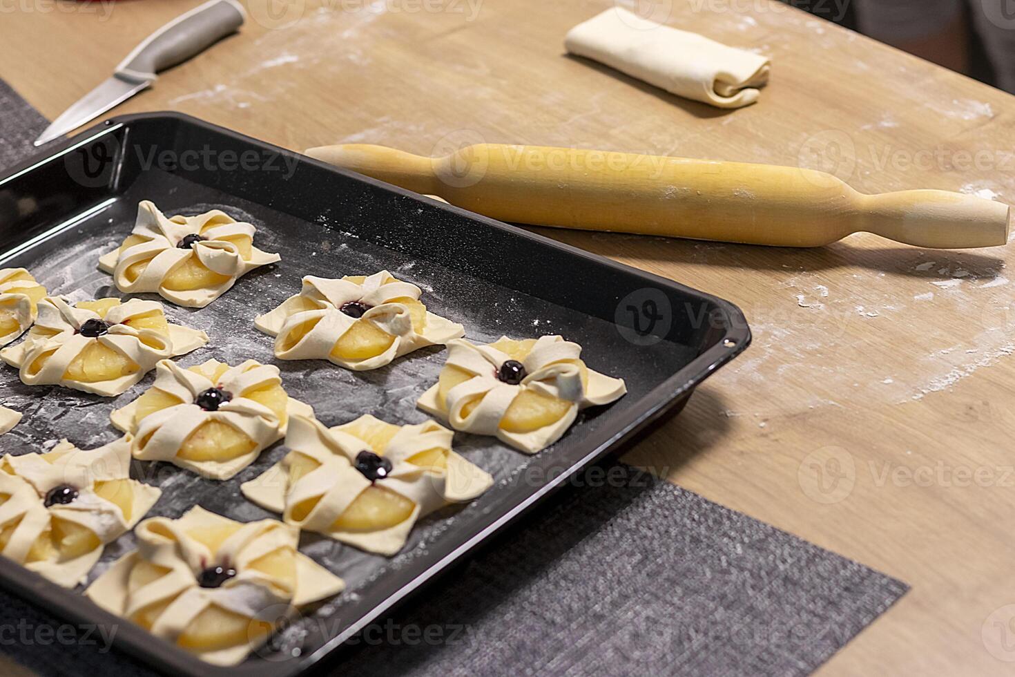 Puff pastry with pineapple wedges wrapped and cherry on top, on the baking tray in the kitchen counter top. Baking, nutrition photo