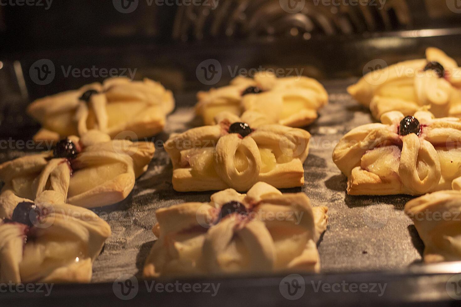 Puff pastry with pineapple wedges wrapped and cherry on top, on the baking tray baking in the oven. Food, hobby, indoor photo