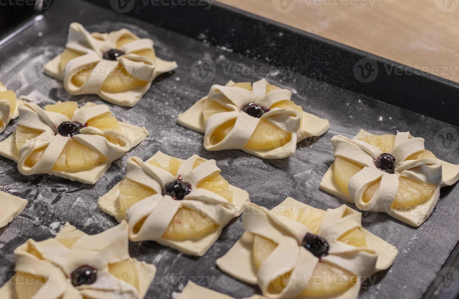 Puff pastry with pineapple wedges wrapped and cherry on top, on the baking tray in the kitchen counter top. Baking, hobby photo