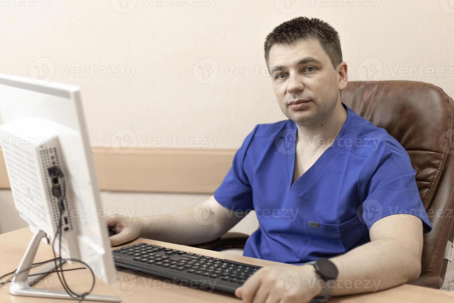 A male doctor in a blue suit is sitting at a computer photo