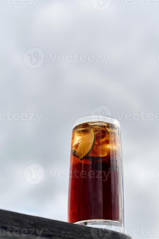 A glass of cola with ice cubes on the background of the sky photo