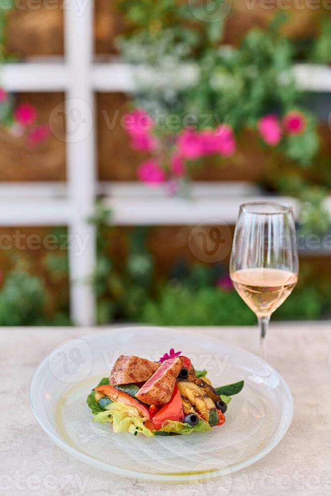 Tasty salad with grilled tuna and vegetables served with glass of white wine photo