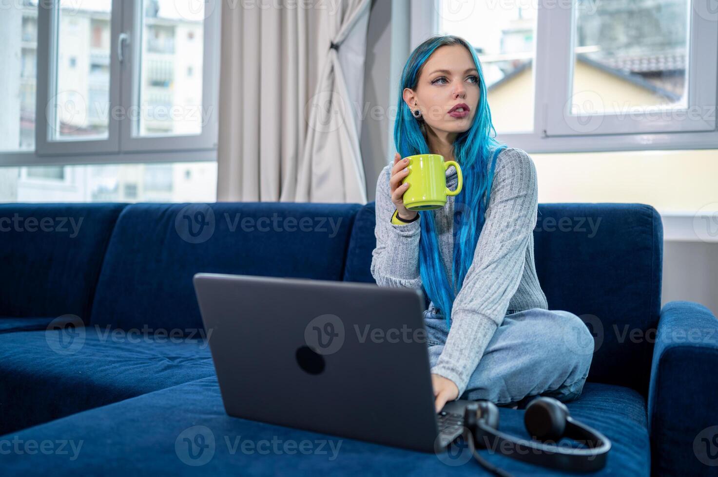 A woman with blue hair sitting on a couch with a laptop. photo