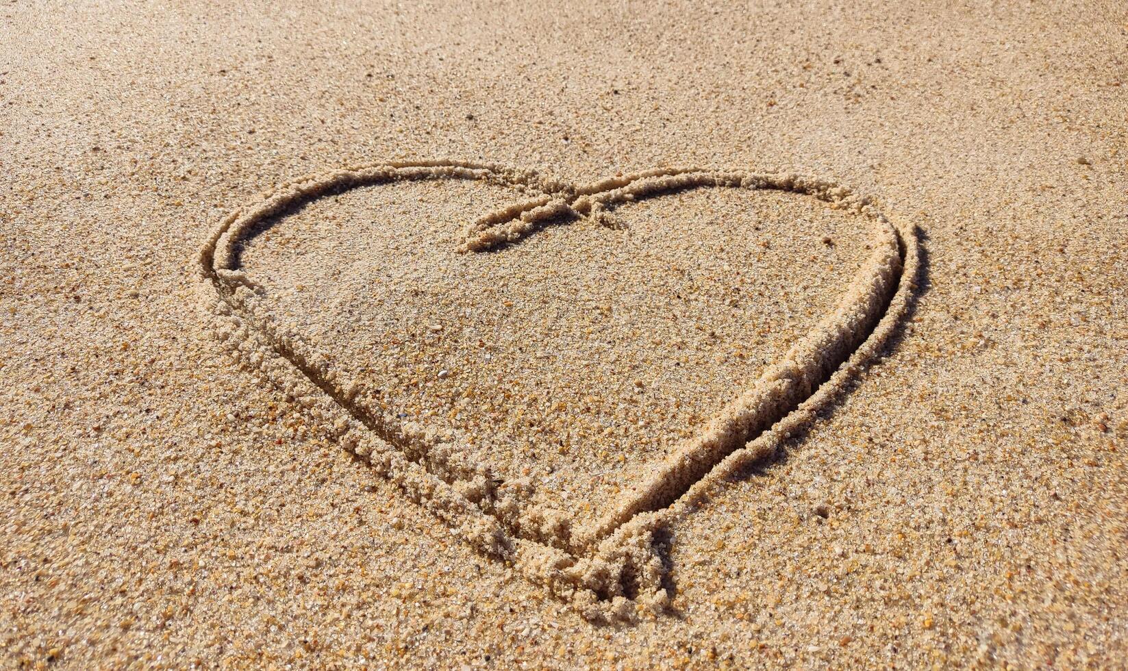 Romantic heart drawn in soft sand on a sunny beach. Perfect for themes of love, holidays, summer, weddings, or destinations. Simple, clean, and heartwarming. photo