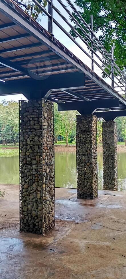 Bridge Columns by the Lake. A pedestrian bridge stands firmly supported by gabion columns over a tranquil lakeside path. photo