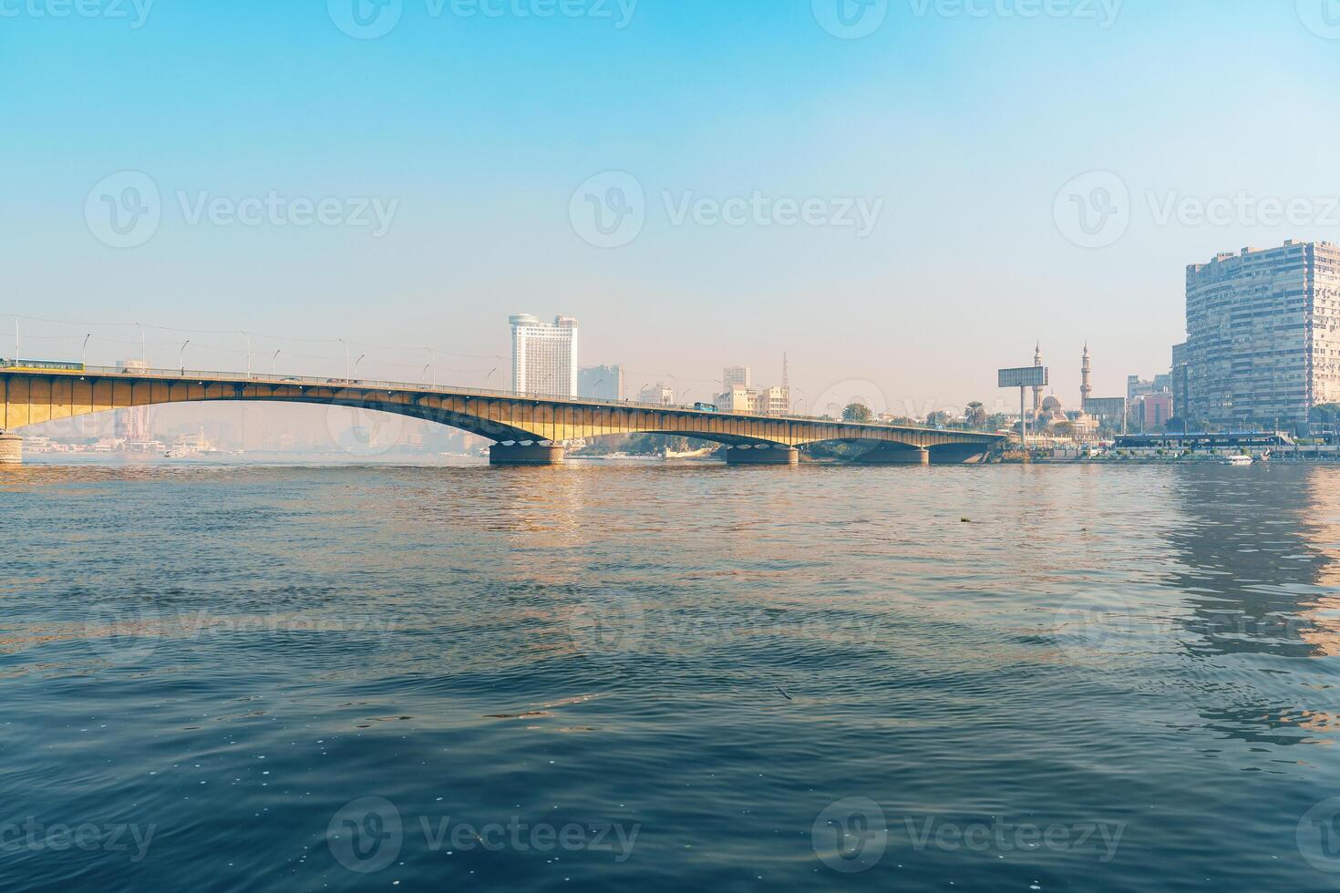 Vibrant view of a bridge crossing a river in a bustling city during a sunny day photo