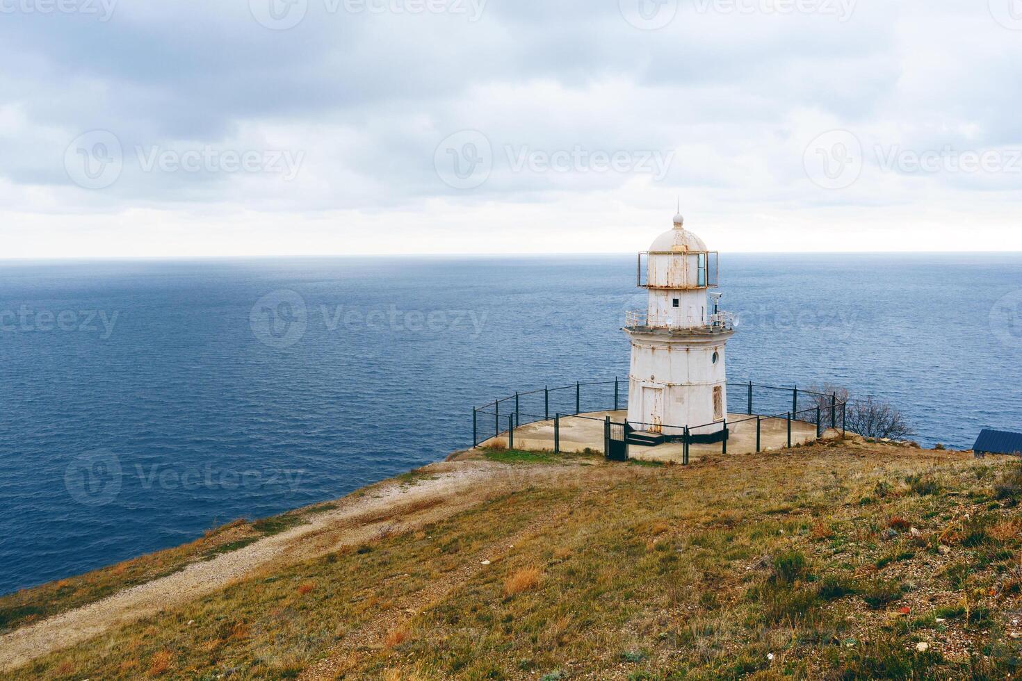 Lighthouse overlooks vast ocean under cloudy sky along coastal landscape in late afternoon photo