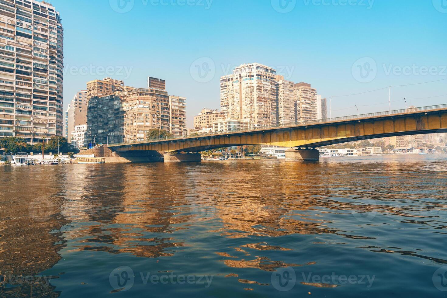 Cityscape view of a bridge spanning the Nile River with modern buildings along the waterfront in Cairo during a clear day photo
