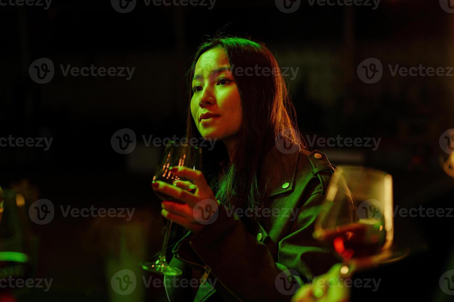 Woman enjoying a drink during a lively gathering in a dimly lit setting with vibrant green lights at night photo
