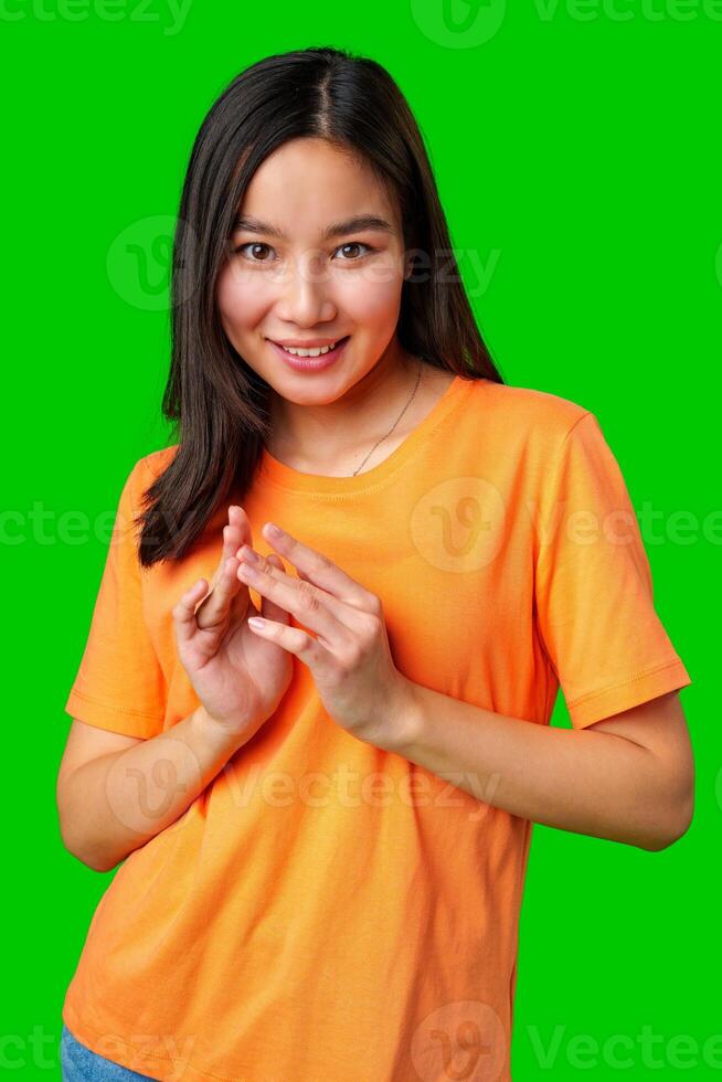 Smiling young woman in orange shirt gestures playfully against a bright green background in a casual setting photo