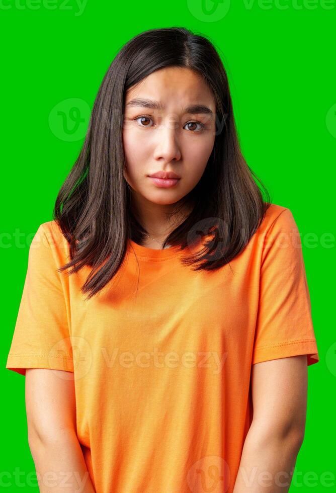 Young woman in orange shirt expressing uncertainty against a bright green background photo