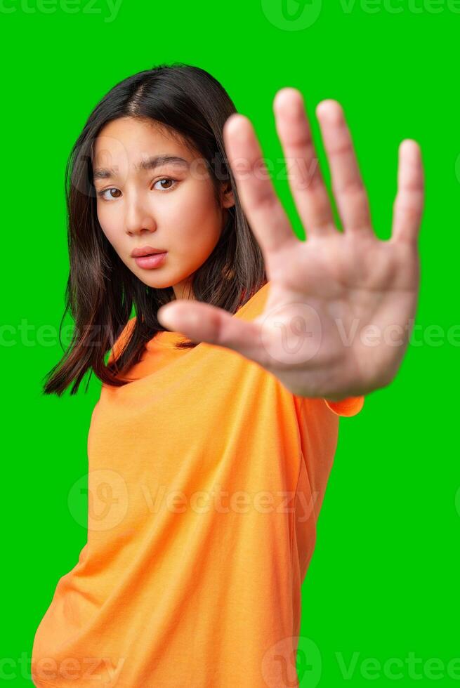 Young woman in orange shirt poses with hand raised against bright green background photo