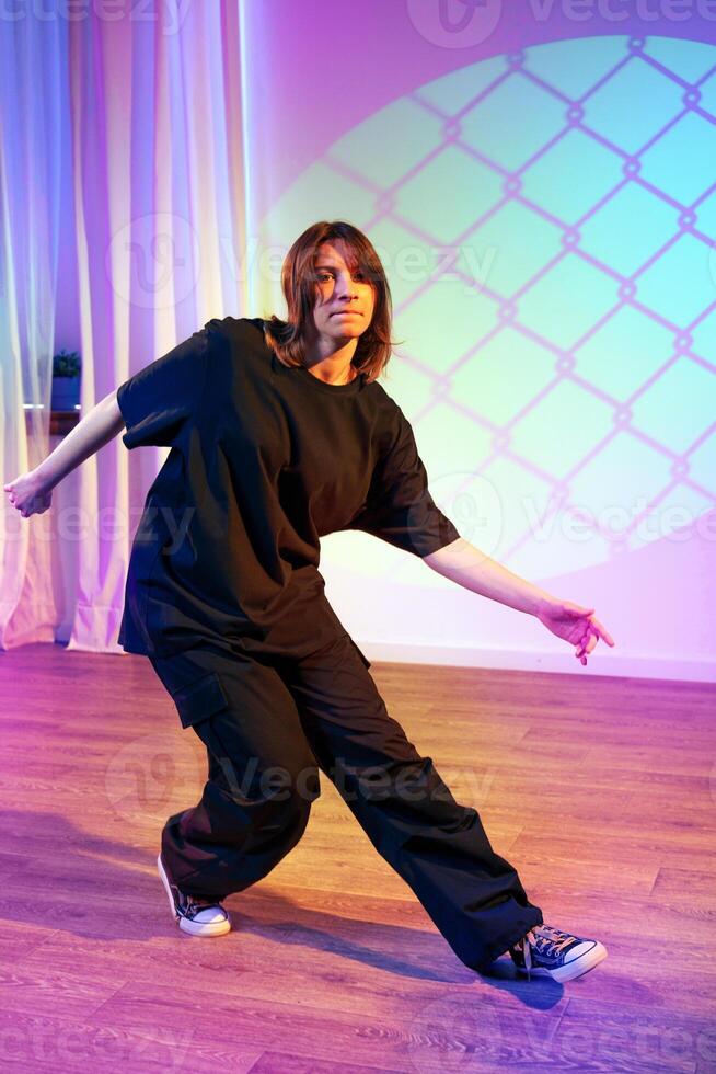 Person dances in stylish black outfit under colorful stage lights in a vibrant studio setting photo