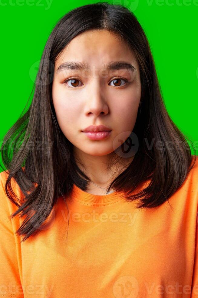 Young woman with long dark hair expresses surprise against a bright green background photo