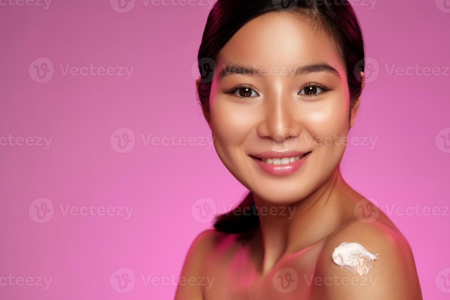 Woman applying skincare cream with a radiant smile in a vibrant pink setting during daylight photo