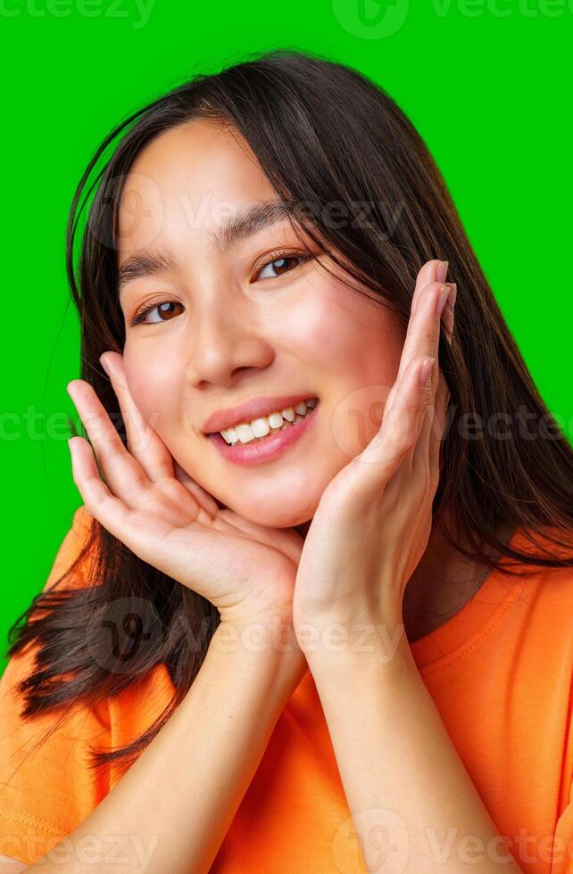 Smiling young woman with long hair poses with hands on her face against a vibrant green background photo