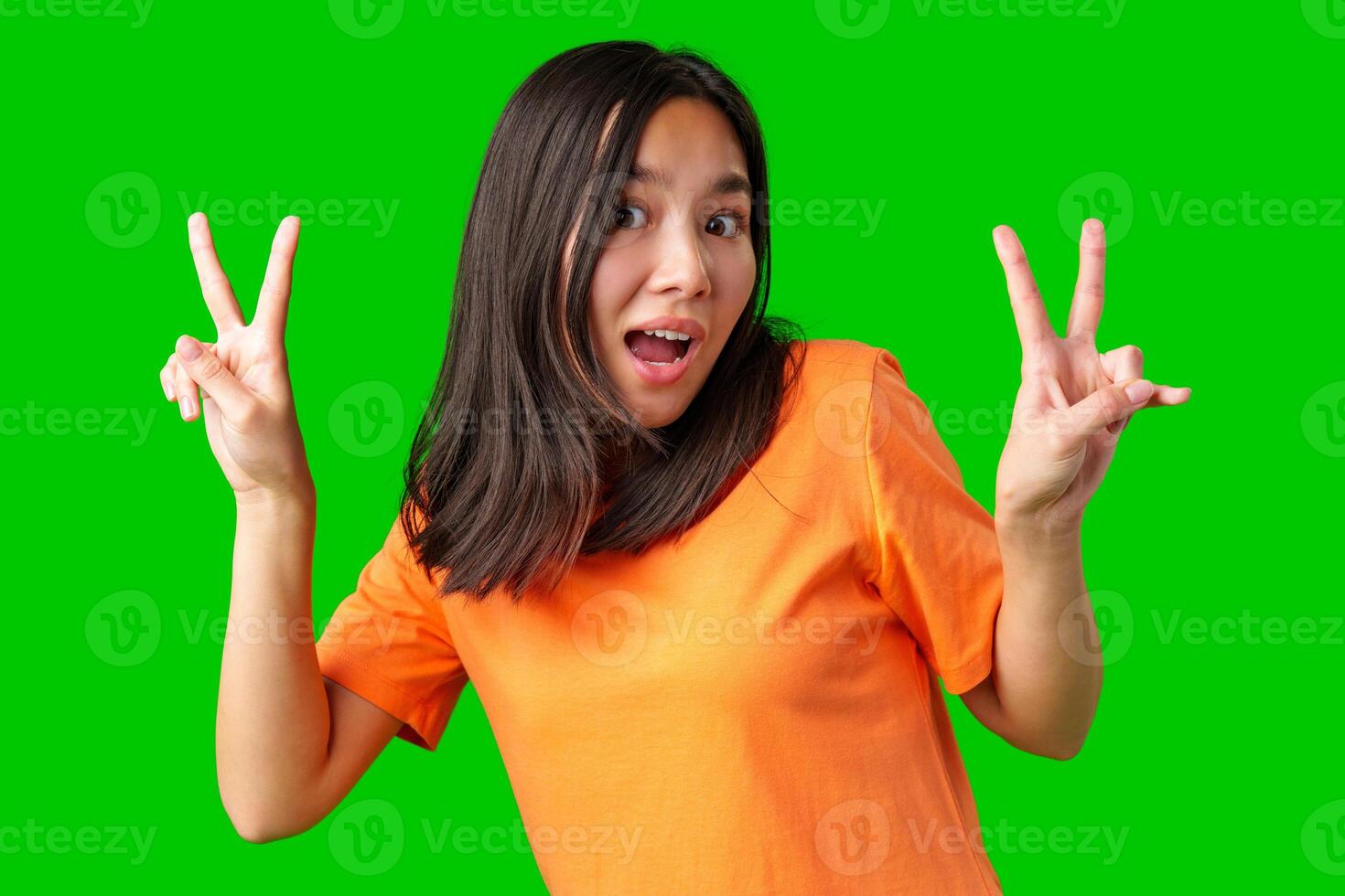 Young woman in orange shirt making peace signs against bright green background during a joyful moment photo