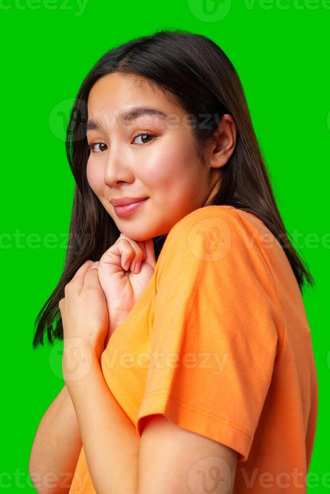Young woman poses playfully against a bright green background wearing an orange shirt photo