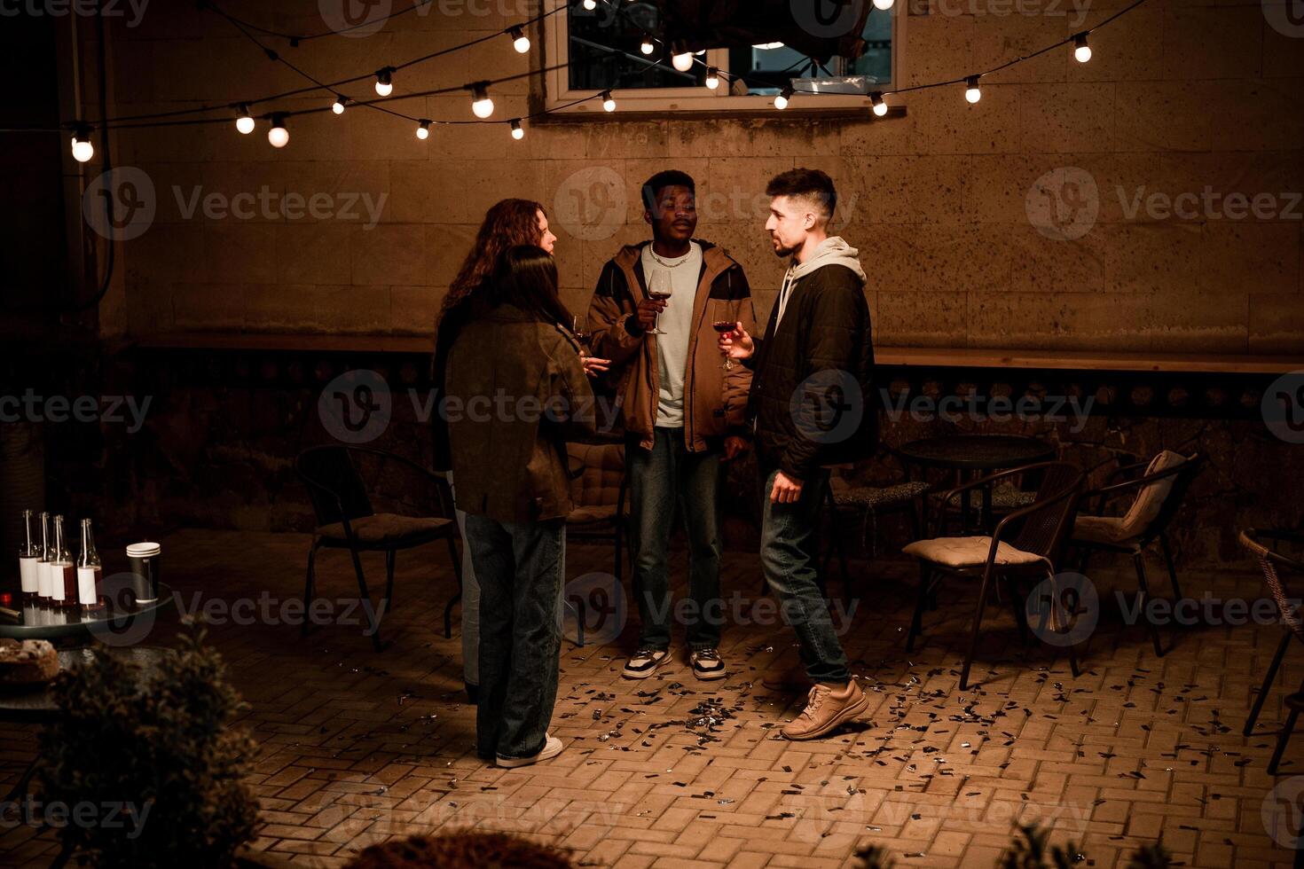 Friends enjoy a relaxed evening gathering with drinks under warm string lights in a cozy outdoor setting photo