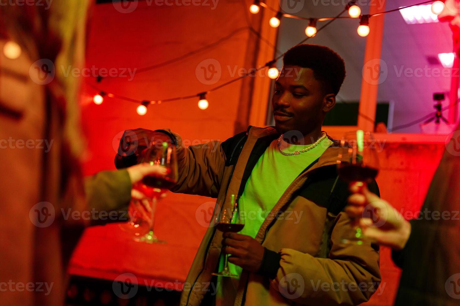 Friends gather at a lively gathering exchanging drinks under warm lights in a colorful atmosphere photo