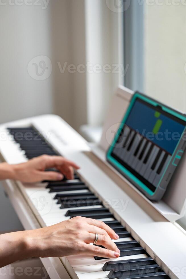 Hands playing a keyboard while following an interactive learning app on a tablet. Technology enables self-education in music without traditional lessons. High quality photo