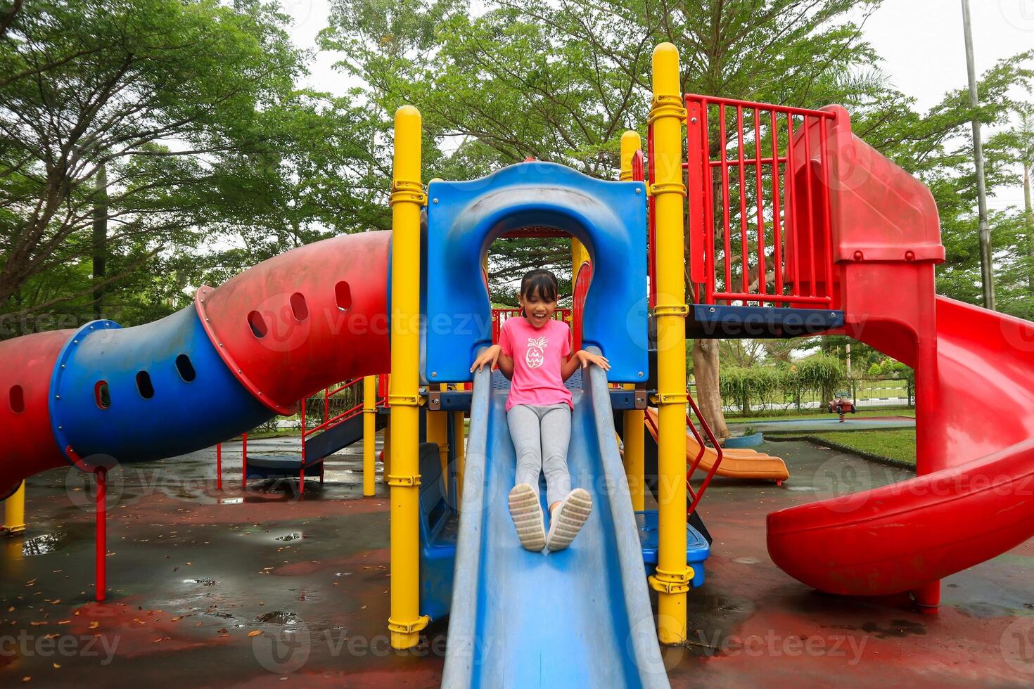 A little Asian girl playing on a slide in a playground photo