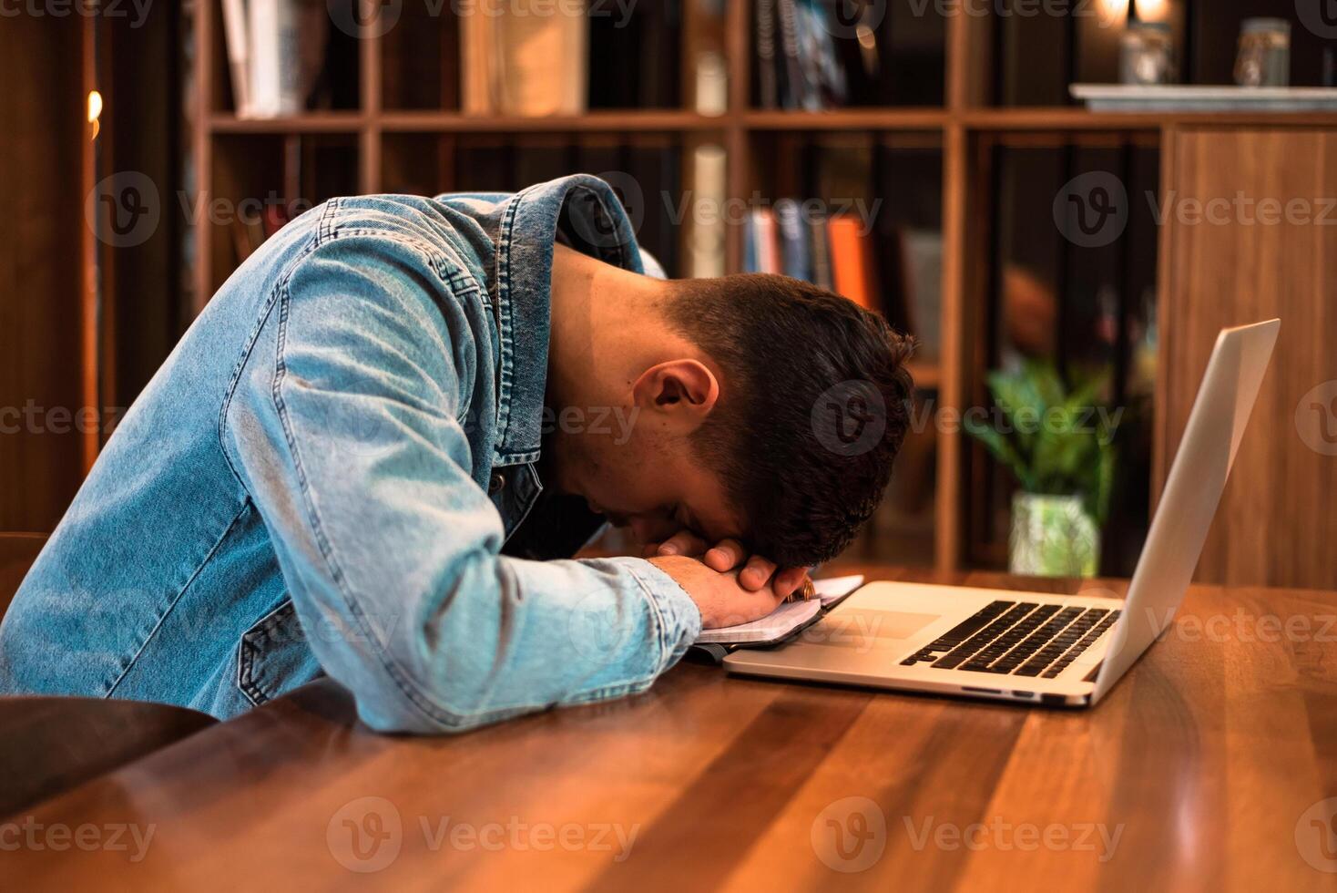 A tired student sleeping on the table while studying or working inside university library or office. photo