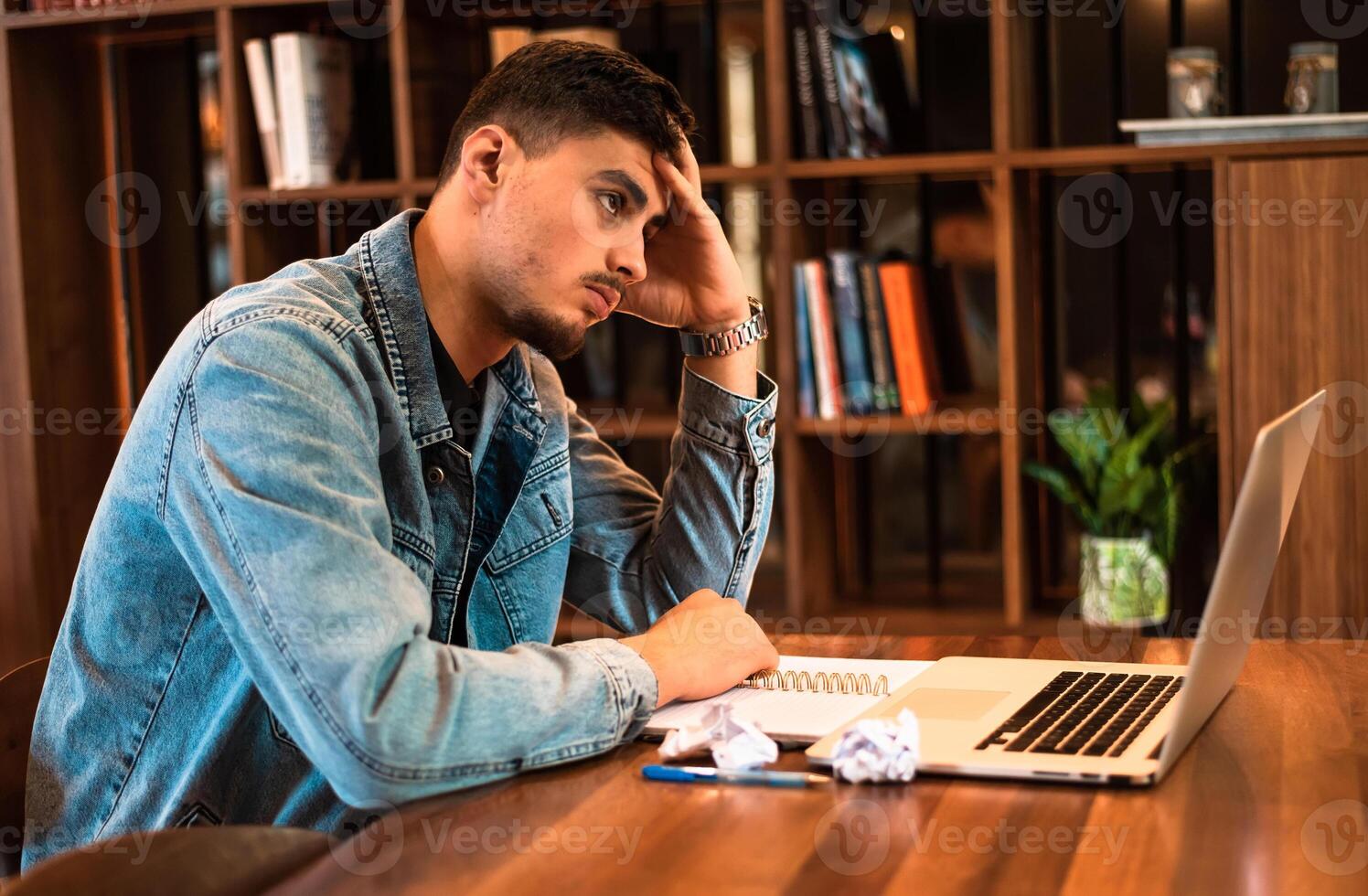 Tired male student crumples up the paper while studying inside university library. A stressed man working in the office or home workplace. photo