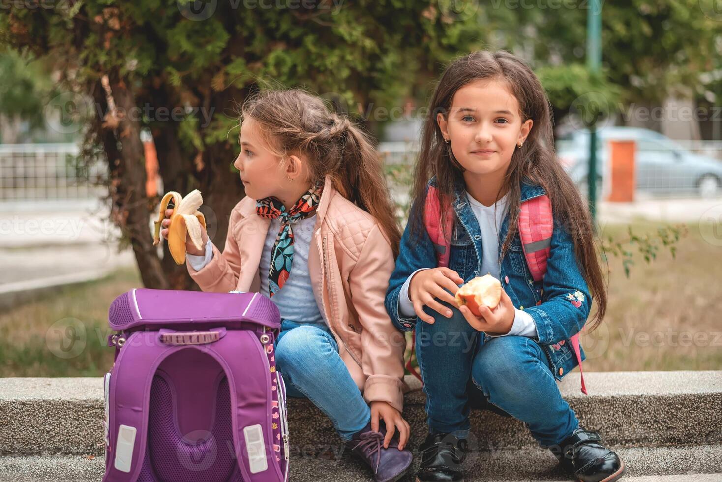 Two child girls on a school lunch break in the yard eating a healthy breakfast. photo