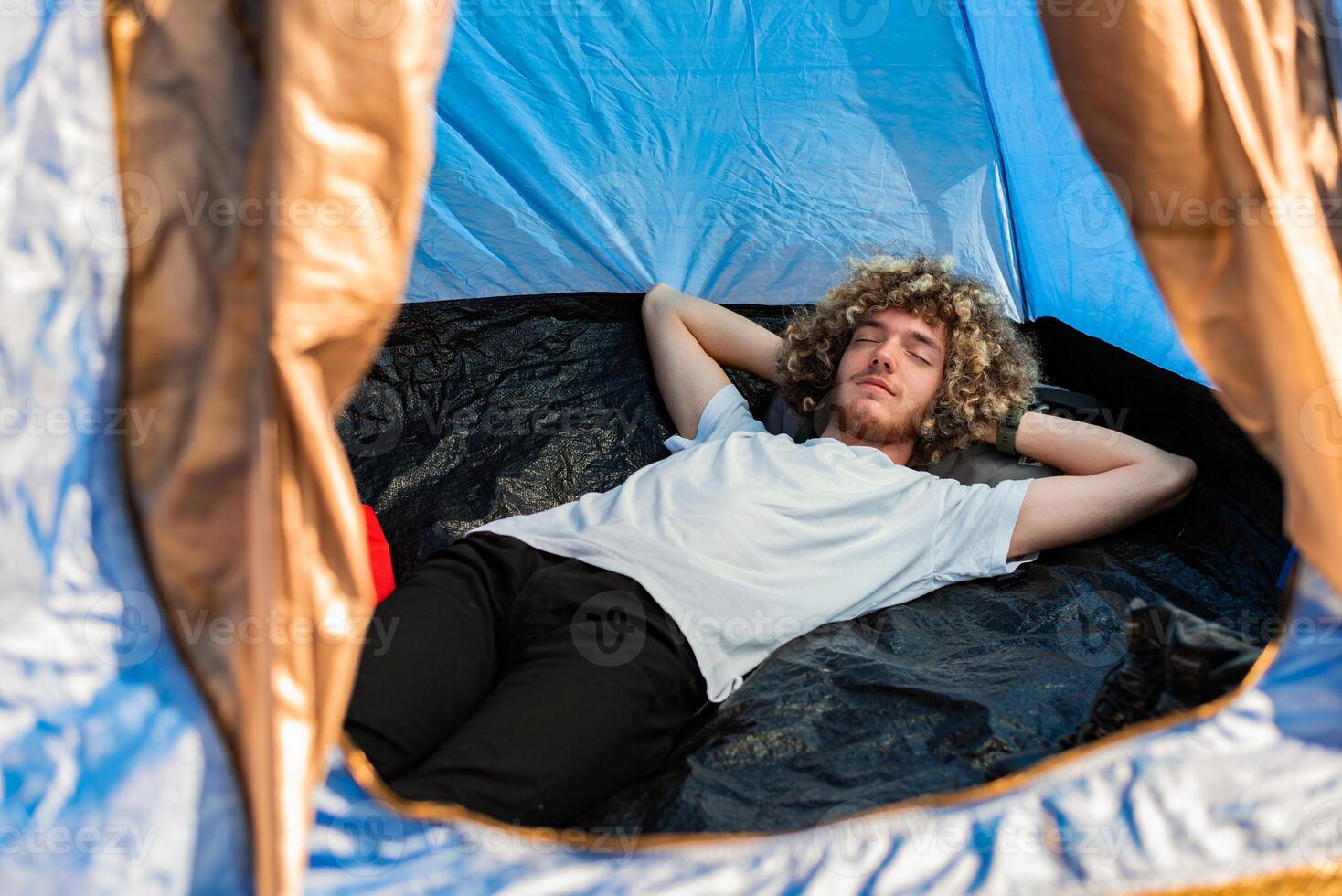 A young man lying with closed eyes in a camping tent. Happy sleeping. photo