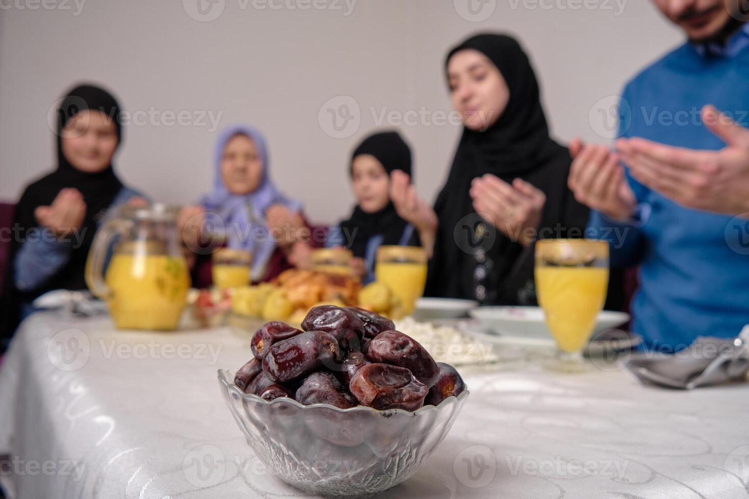 Happy Muslim family together making iftar dua to break fasting during Ramadan at home dining table at home focus on a bowl of dates healthy nutrition during the fast. photo