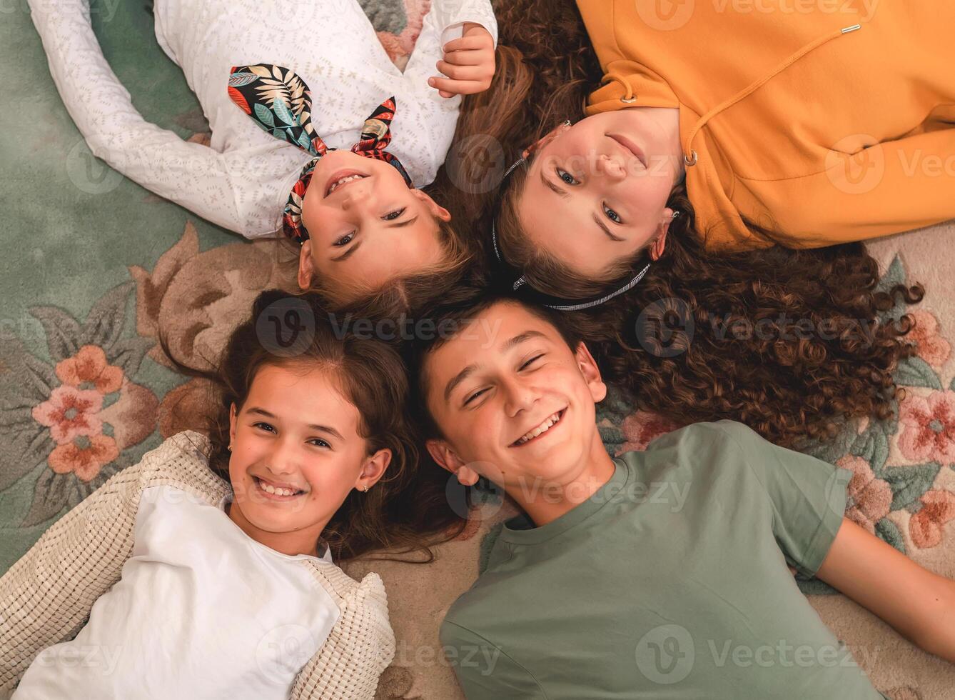 Happy group of children friends lying on the floor in a circle, looking at the camera, top view. photo