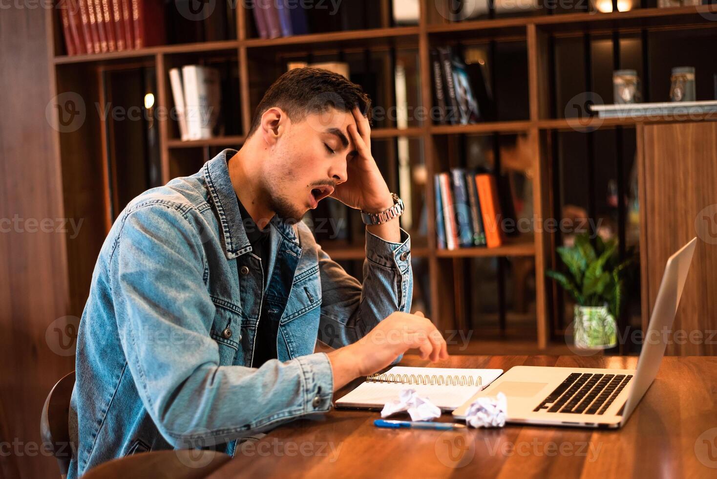 A tired student yawning while studying inside university library. photo