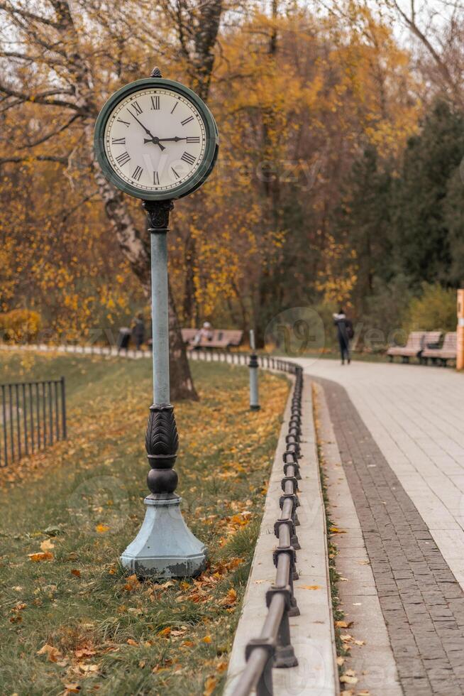 Classic clock stands tall in park surrounded by autumn leaves on a quiet afternoon photo