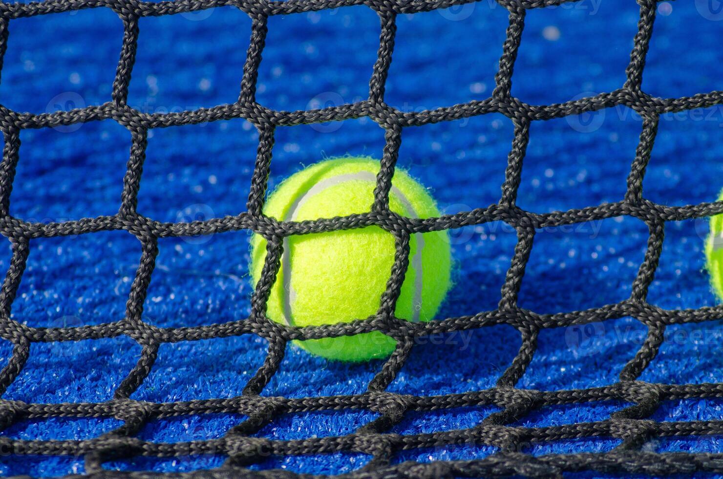 isolated padel ball behind the net in a blue paddle tennis court, background for racquet sport concept photo