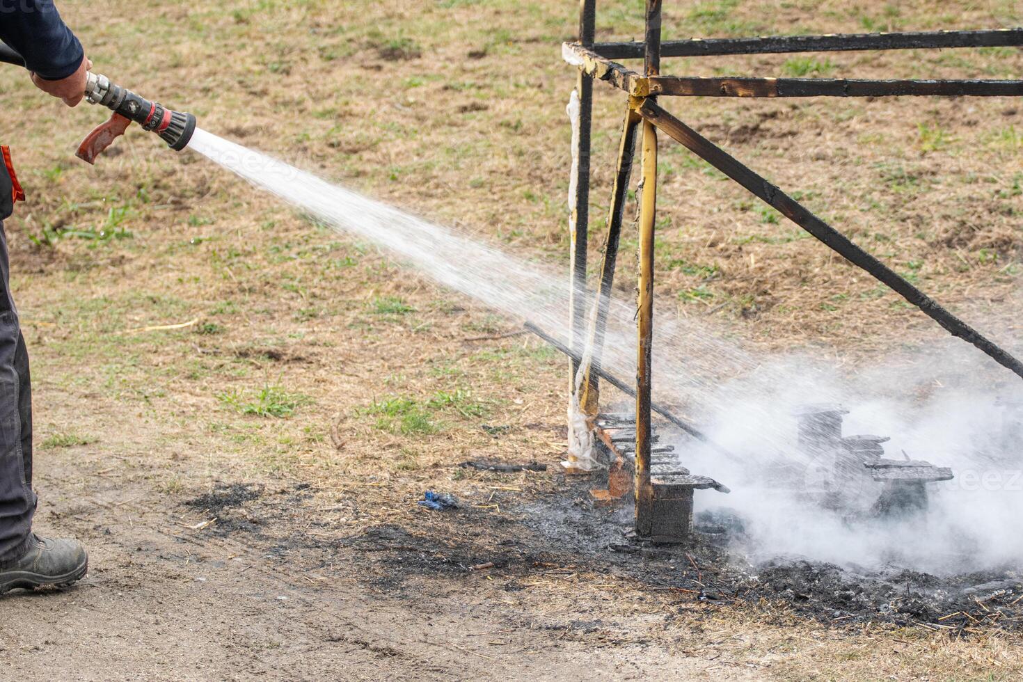 firefighter extinguishing smoldering wood structure with hose firefighter managing hot spots on burnt structure remains photo