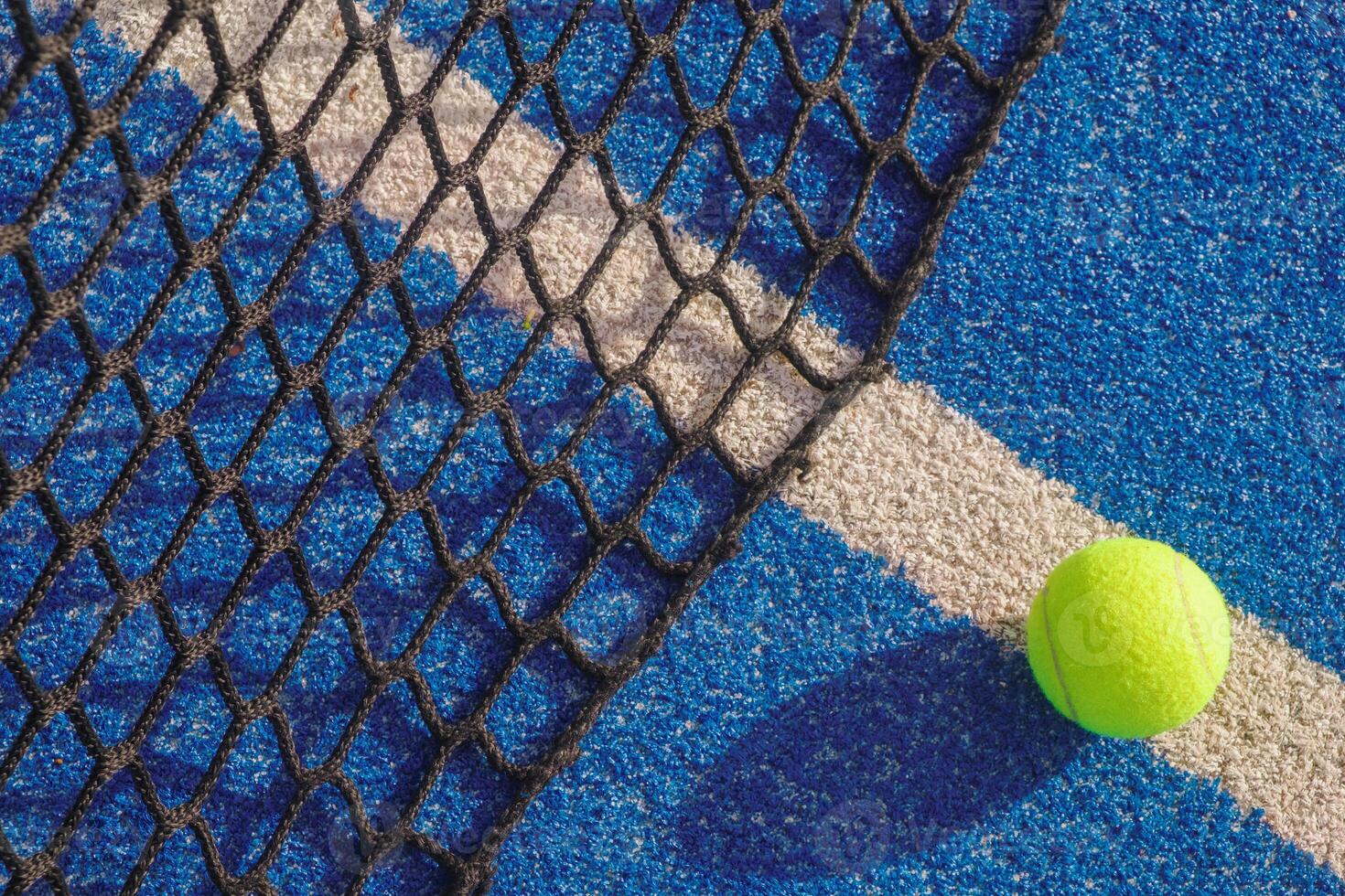 selective focus, a ball on the line next to the net in a blue paddle tennis court photo
