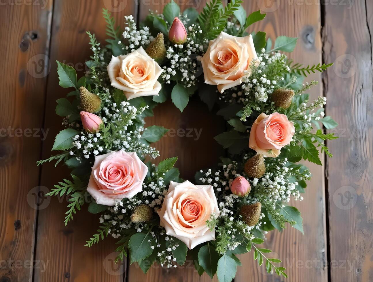 A wreath of pink roses, greenery, and white flowers hangs against a rustic wooden backdrop photo