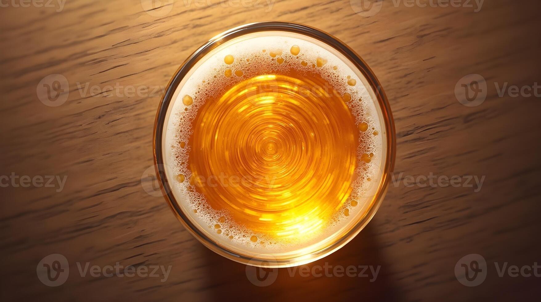 A top-down view of a glass of beer with a swirling pattern in the foam, set against a wooden table backdrop photo