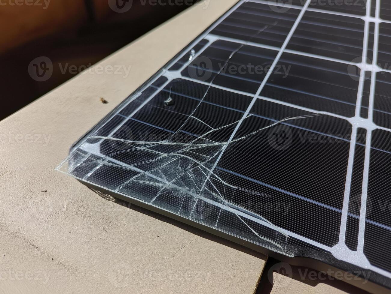 solar panel with cracked glass lies surface, showcasing damage and wear. sunlight reflects off broken surface, highlighting fragility of solar photo
