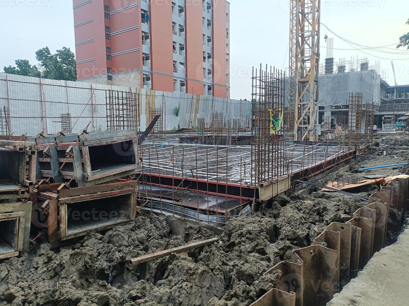 Construction site with foundation work, steel reinforcement, and building materials visible, showcasing urban development and progress photo