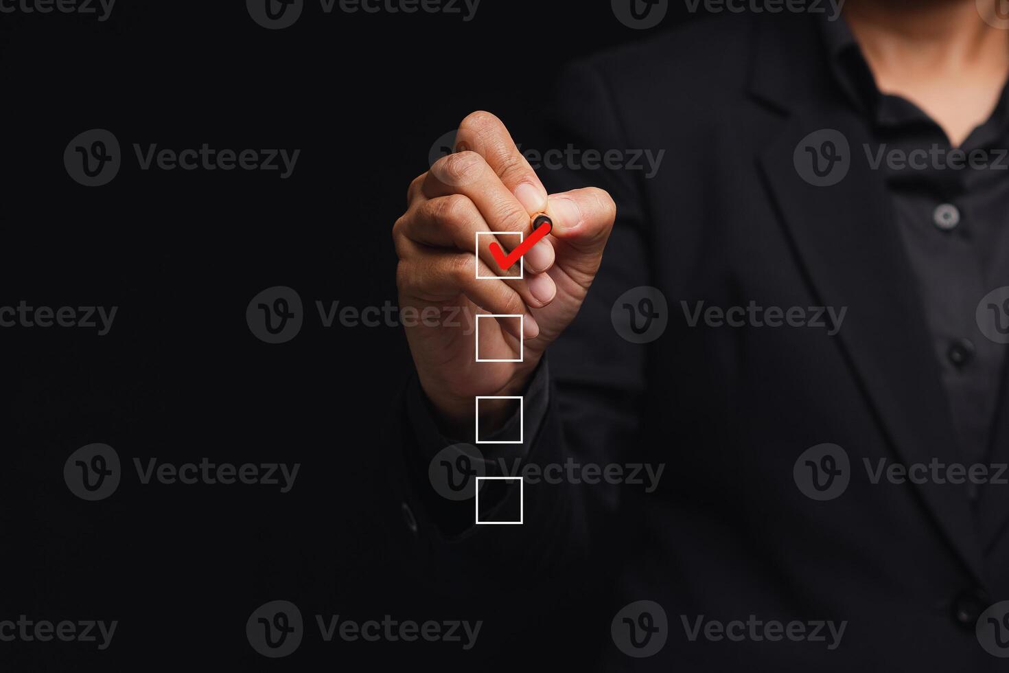 Businessman holding a pen and checking a mark on the boxes symbol is one of four options while standing on a black background photo