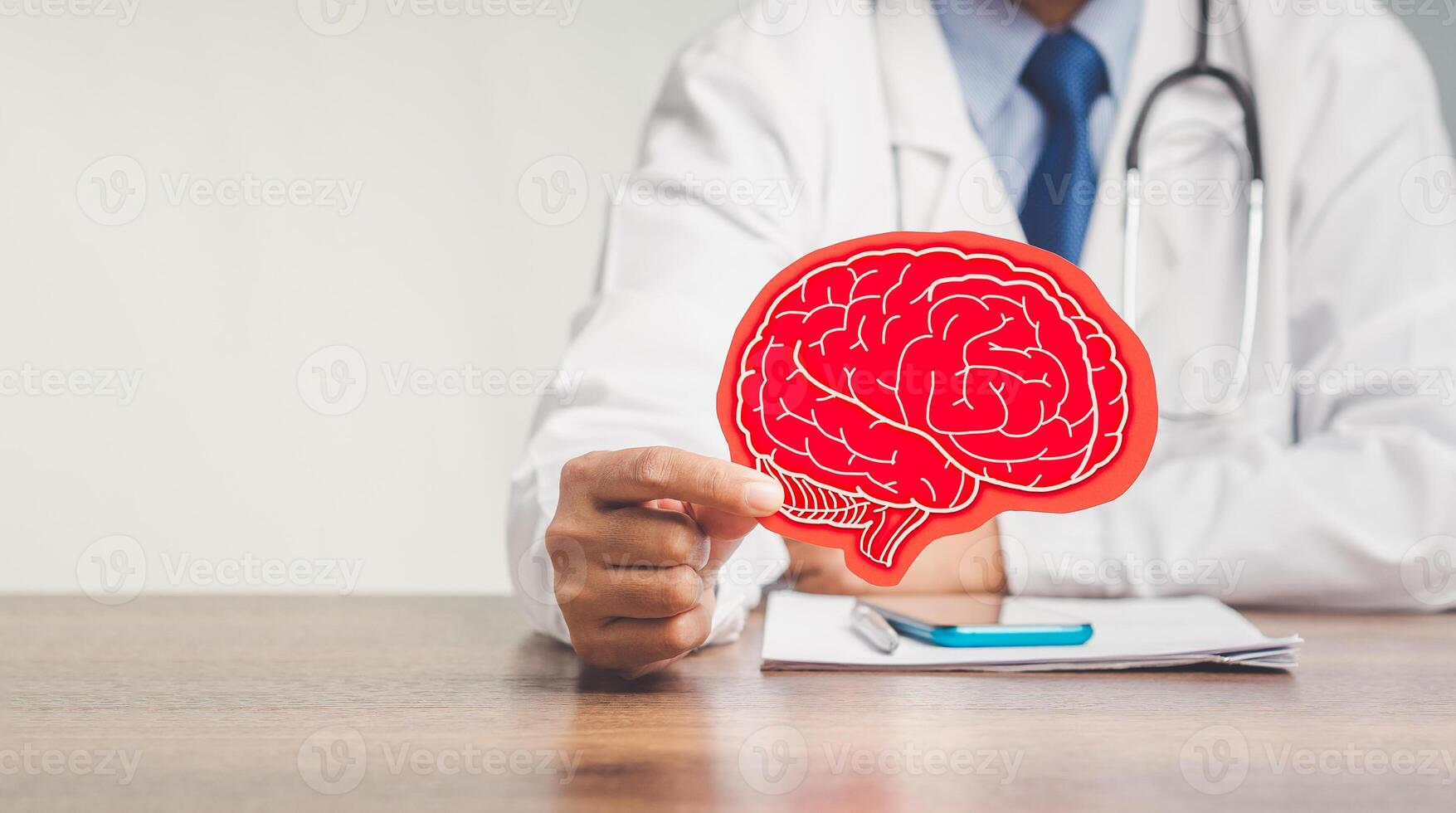 Close-up of a doctor holding a brain symbol made from red paper while sitting at the table in the hospital. Space for text. photo
