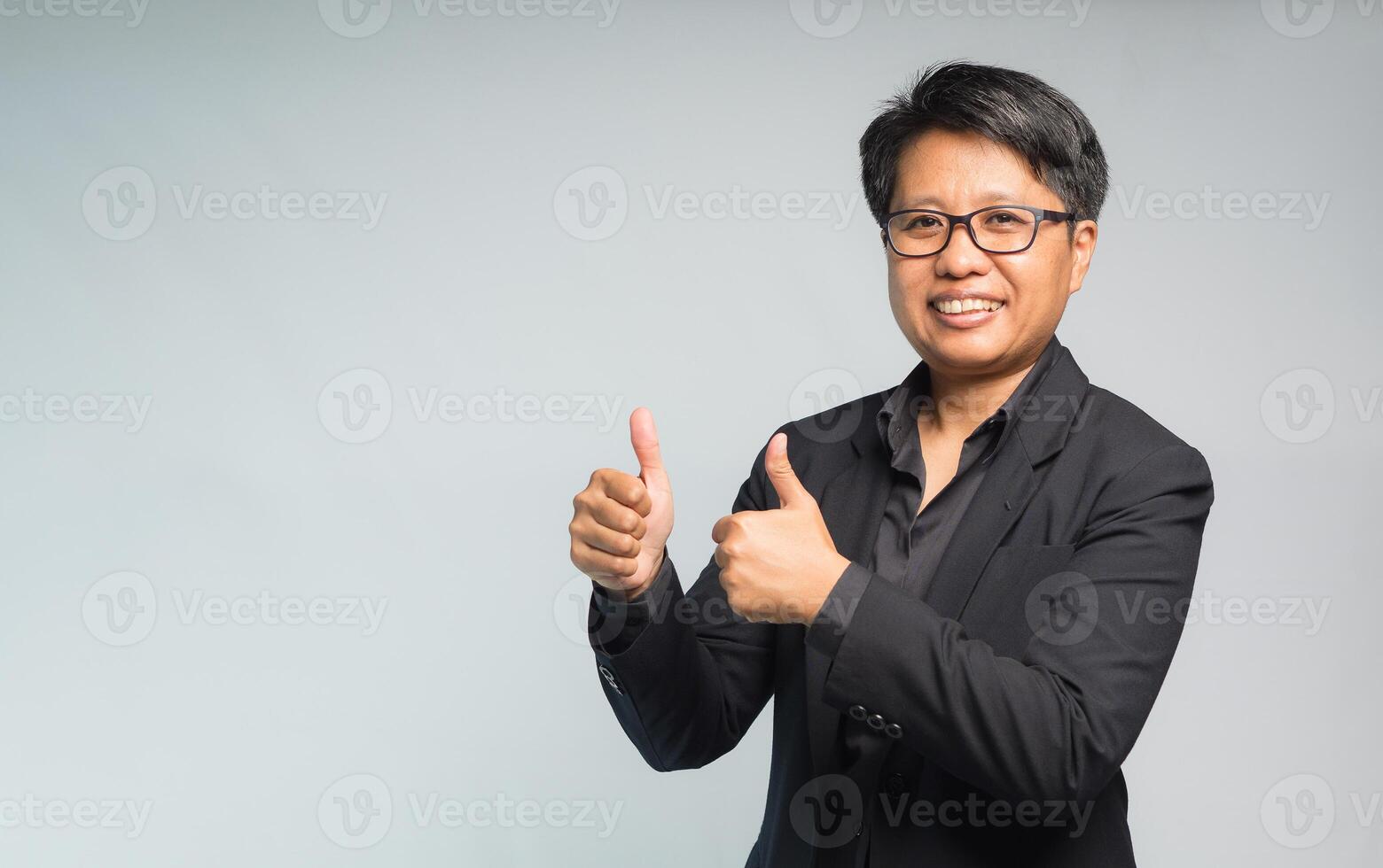 Portrait of a businesswoman with short black hair in a suit hands showing thumbs up while standing on a gray background photo