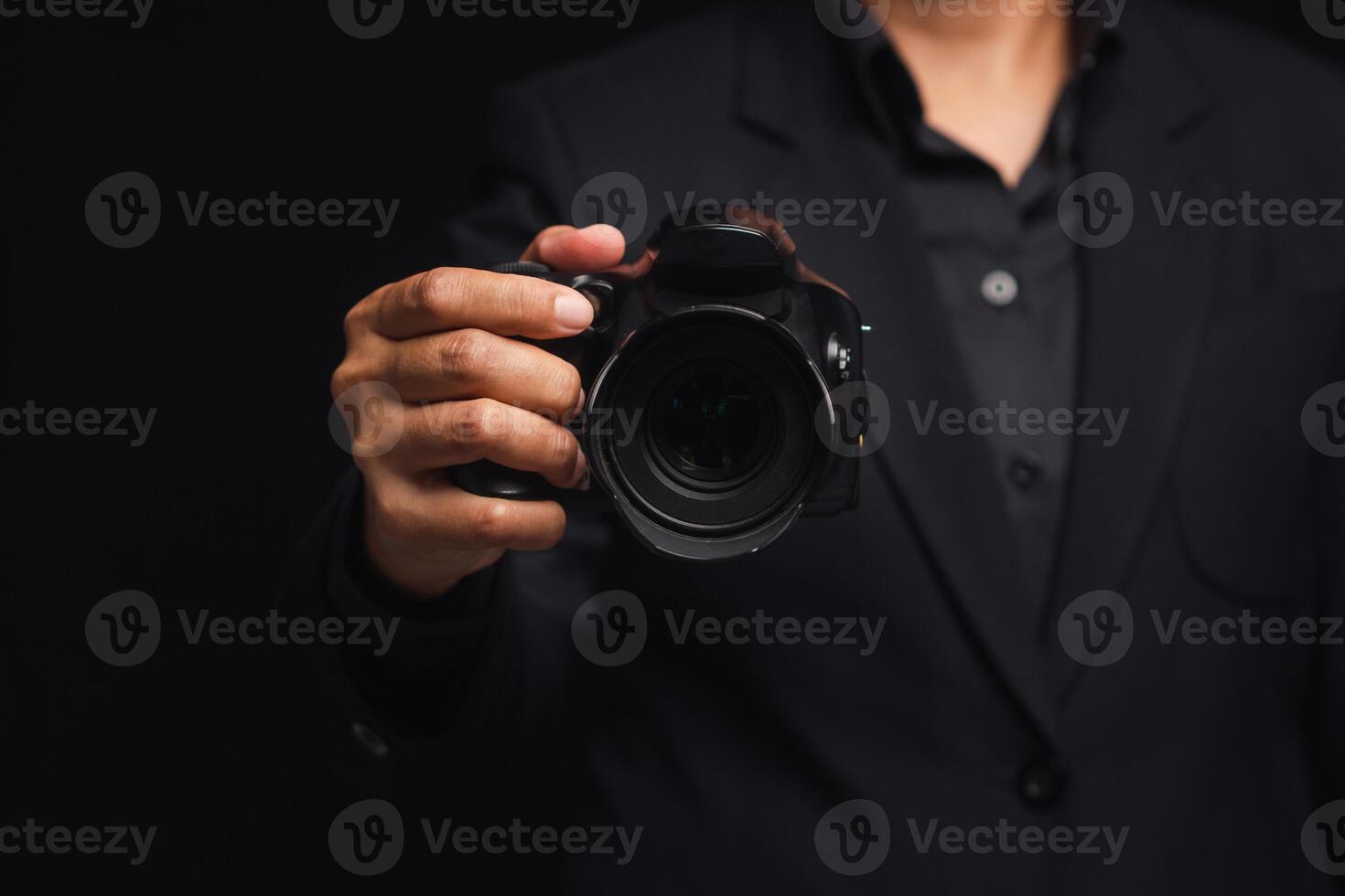 Photographer in a suit holding the digital camera while standing on a black background. photo