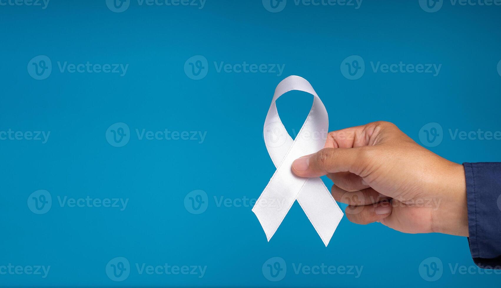 Hand holding a white ribbon symbol the fight against lung cancer on a blue background photo