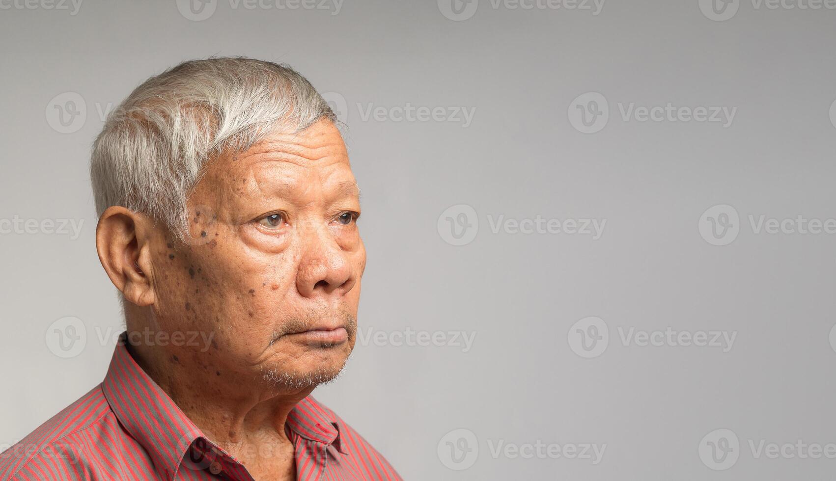 Portrait of an elderly Asian man in a shirt looking away with a smile while standing on a gray background photo