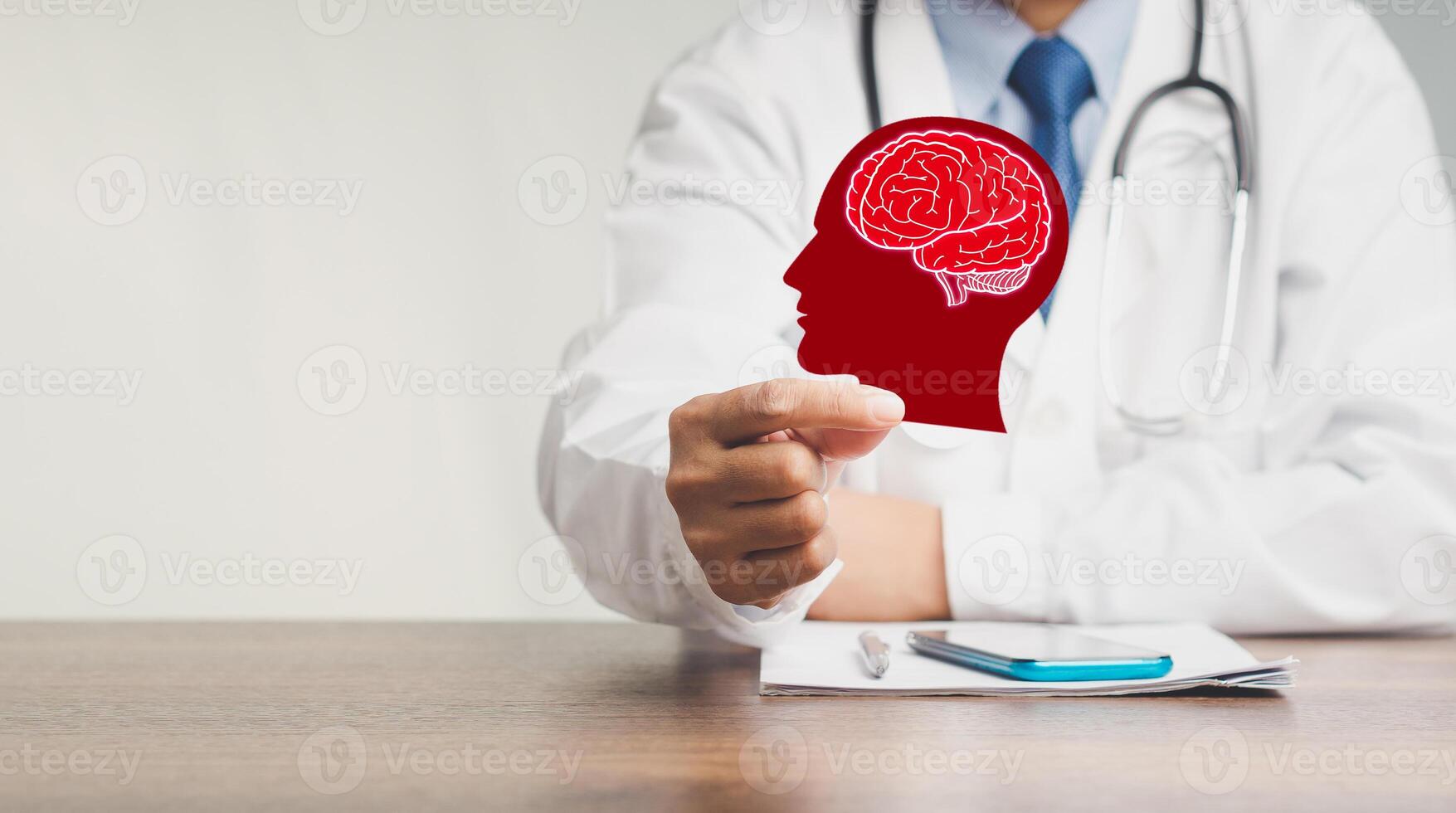Doctor holding a brain symbol made from red paper while sitting at the table in the hospital. photo
