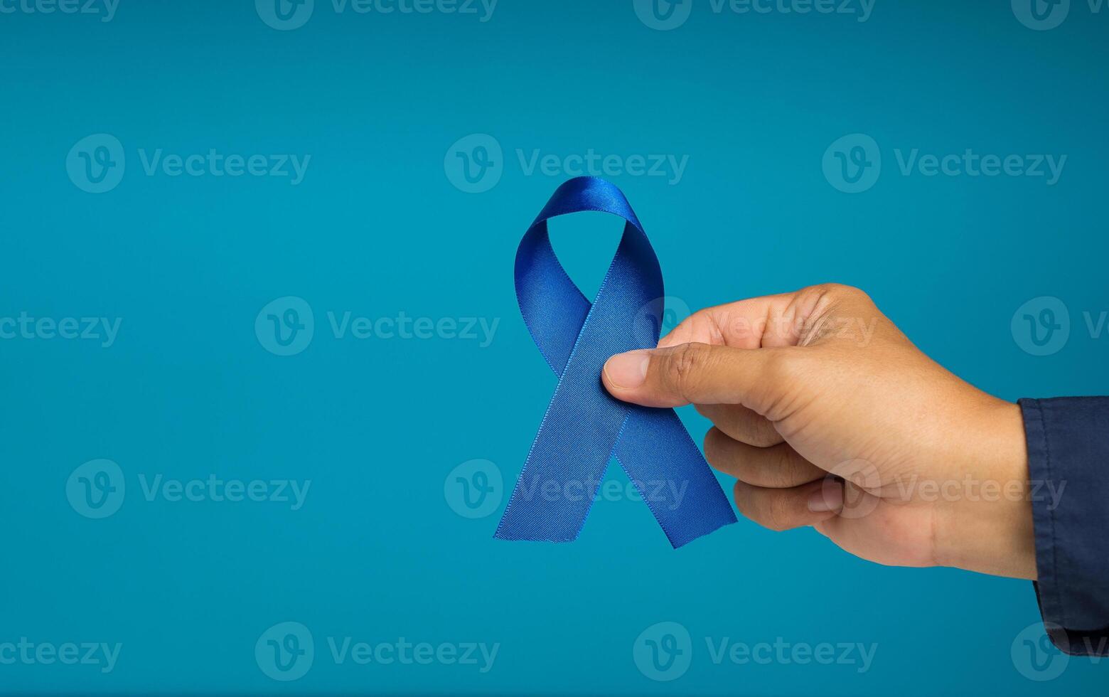 Close-up of a hand holding a blue ribbon symbol against a blue background photo