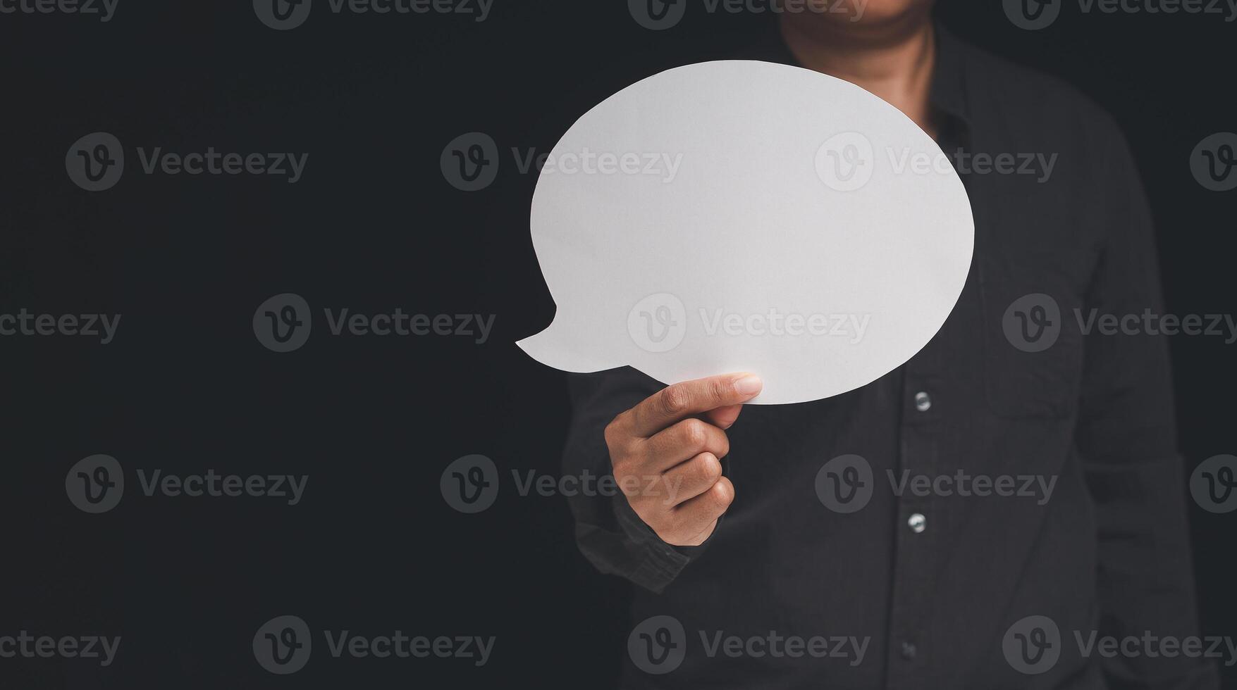 Close-up of a businessman holding a blank white speech bubble while standing on a black background photo